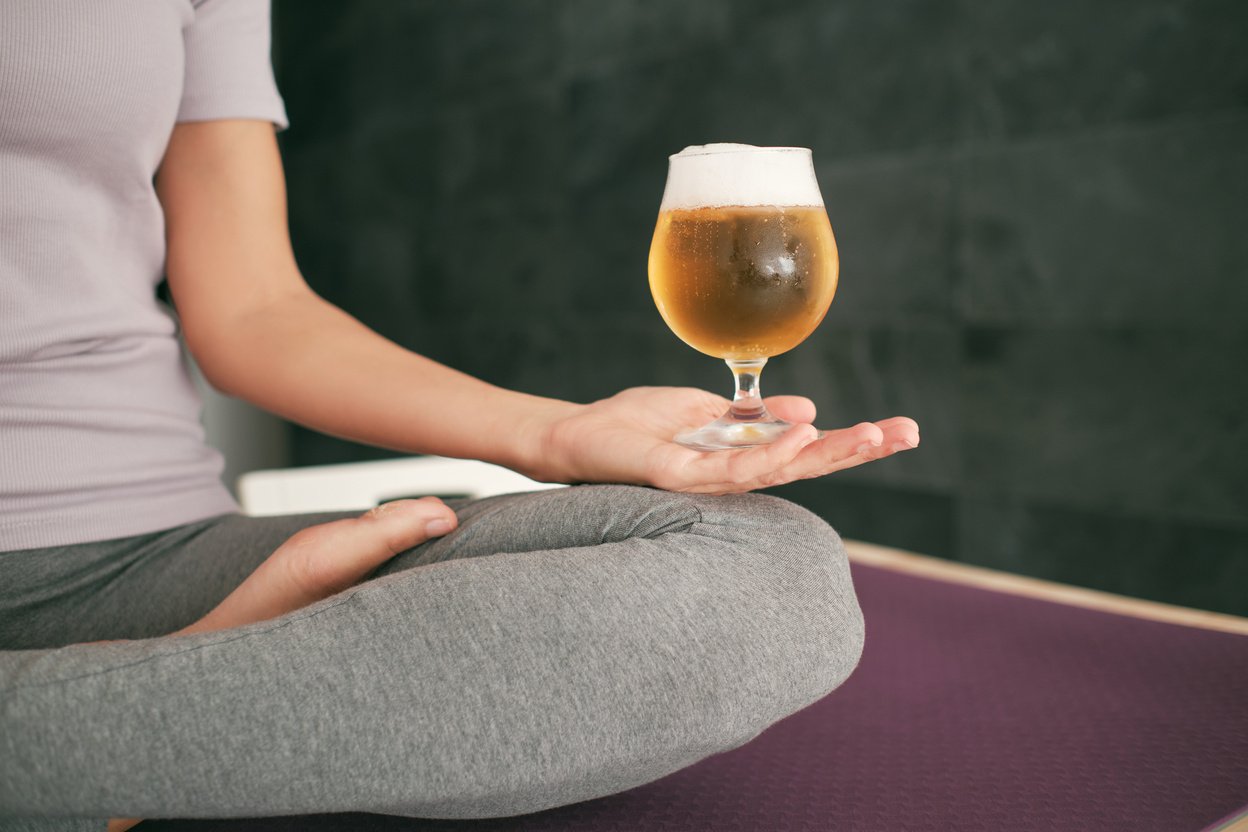 Unrecognizable woman practicing yoga with beer